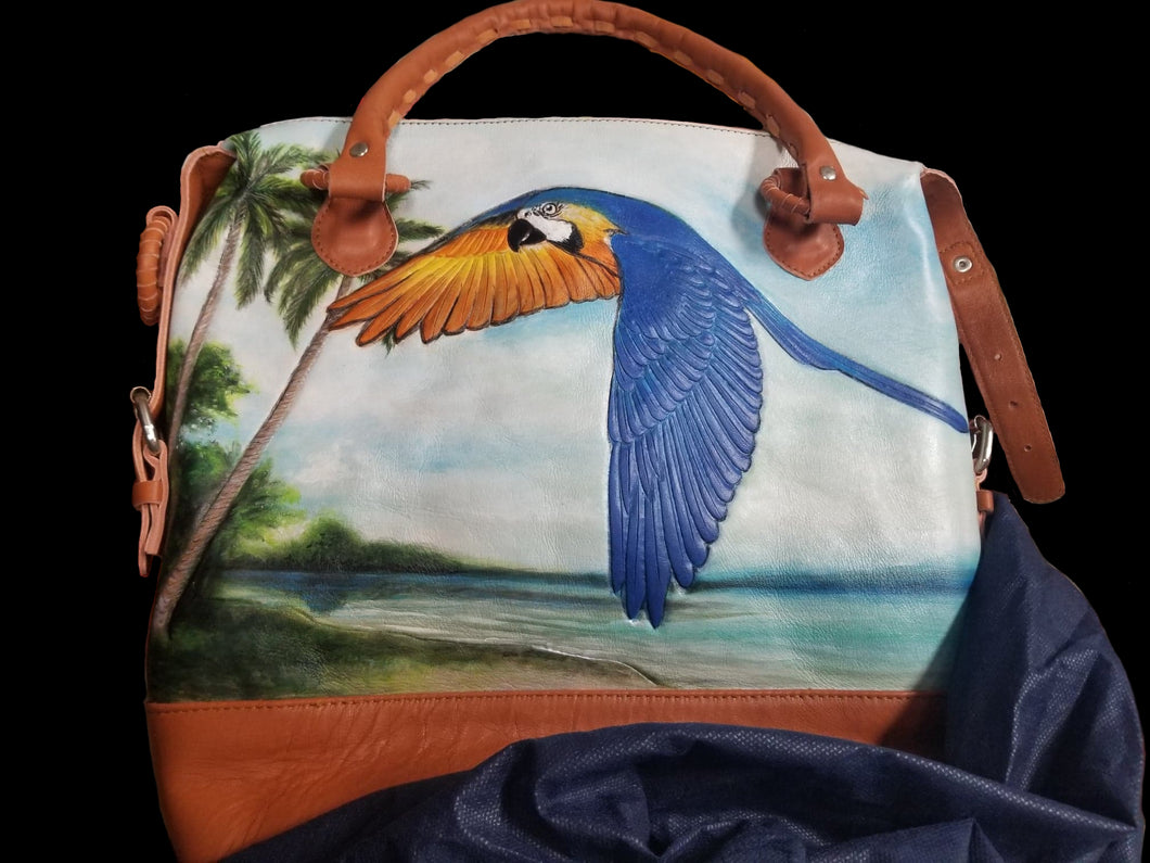 Front of the handtooled, handpainted leather bag featuring a Blue & Gold macaw flying along a tropical beach.