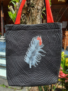 A handpainted batik shoulder bag with an African Grey (grey & red) feather batiked onto the front of the bag. One handle is red, the other is black. Lightly quilted to highlight the design!
