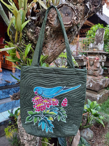 A handpainted batik shoulder bag featuring a blue mutation Indian Ringneck parakeet, perched on red & white flowers. The design is set on a very dark green background