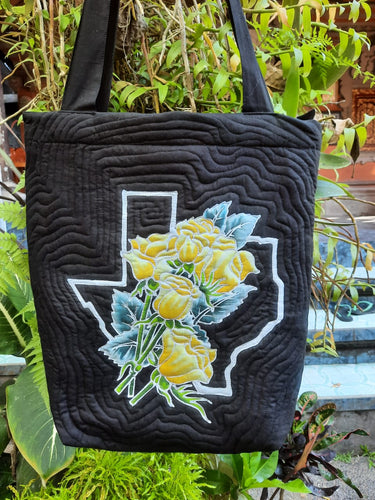 A bouquet of 5 yellow roses exquisitely drawn, batiked, and painted by hand, set against an outline of the  Texas border. The black background ensures a classic look that pairs up beautifully with a special occasion or casual outfit.