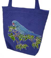 Front view of the handpainted batik Quaker Parrot shoulder bag. This bag features the blue mutation Monk Parakeet perching on green, tropical leaves. The background color is blue.