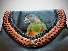 View of the front of the handtooled, handpainted Senegal parrot clutch. From this angle you can see the slight creasing in the leather. The background leather color is black, with 2 rows of decorative trim around the bird.  One row is black trim, and the other is tan-colored V-shaped trim.