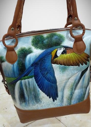 Hand-tooled, hand-painted leather bag of a Blue & Gold macaw flying alongside Brazilian waterfalls. The intricate and detailed tooling and painting are simply works of art!