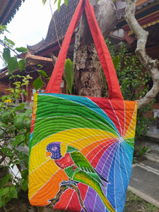 A hand-painted batik tote-style bag of a rainbow lory set against swirling rainbow colors.